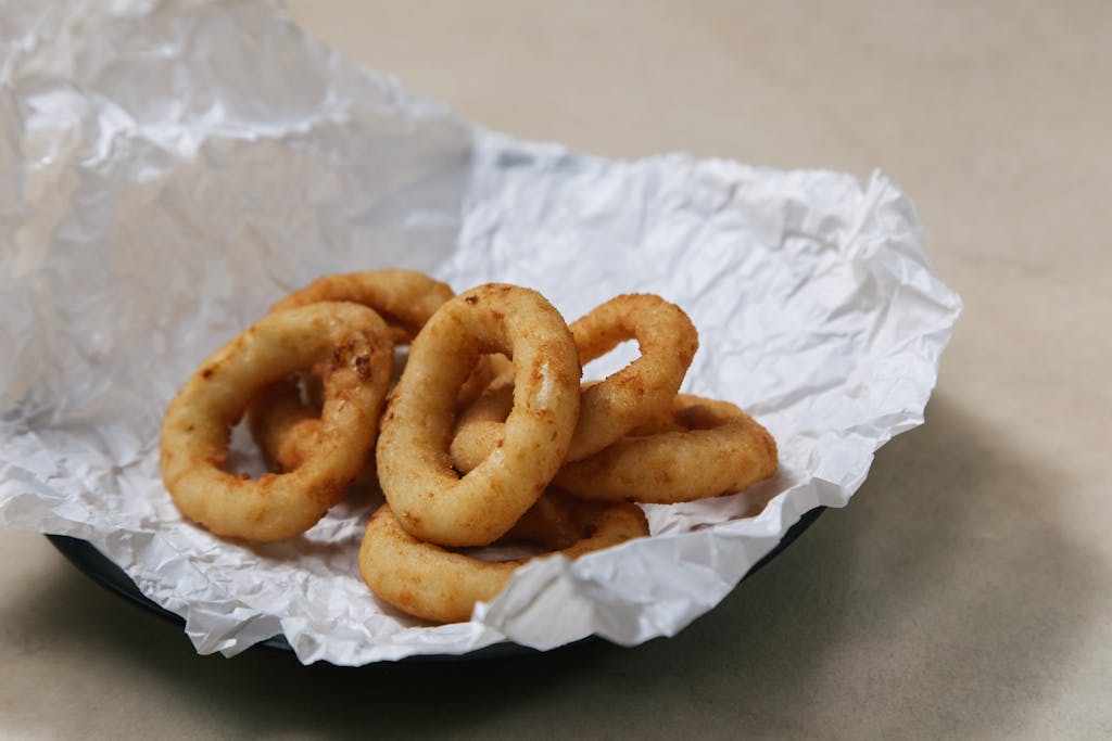 Close-up of crispy golden onion rings served on a crumpled white paper plate.
