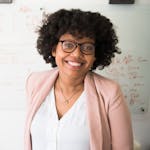 Smiling businesswoman with glasses and afro hairstyle in an office setting.